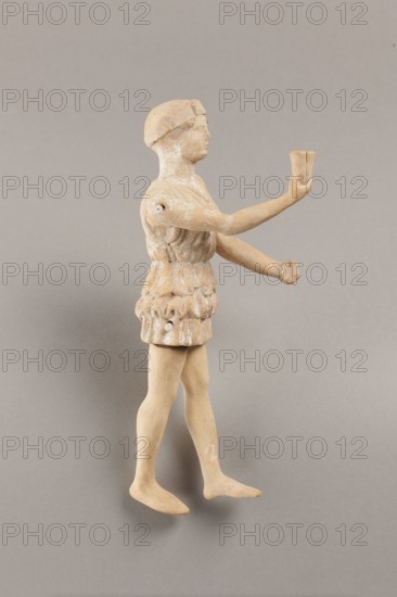 Doll with movable limbs, terracotta, dolls, Made of terracotta. The doll with movable limbs depicts a woman in a short, pleated chiton and a bonnet. In her right hand she holds an instrument resembling castanets. The figure's oval head, directed slightly upwards, is set on a long, rather thick neck compared to the rest of the body. Lush curls protrude from under the headdress. The figurine's movable limbs are long compared to the rest of the body. 4th century BC, Attica according to Weronika Krzemien the object comes from Italy. Figurine, toy. Height 18.9 cm, width 8 cm, depth 3.5 cm, weight 0.13 kg., A small figurine of a person shown in profile standing on a neutral background, primarily in beige and light tan tones with areas of lighter white wear; the figure wears a textured tunic with sculpted folds and a short skirt, has a rounded cap or hair shape on the head, and outstretched arms with one hand holding a small cup-like object; the legs are bare and the feet are flat, and the su...