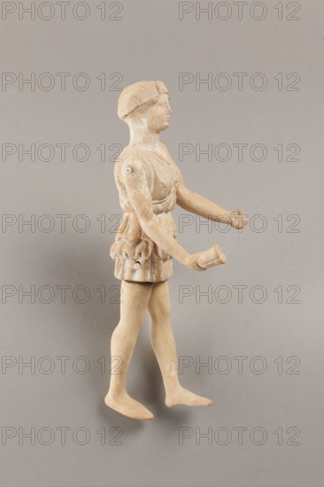 Doll with movable limbs, terracotta, dolls, Made of terracotta. The doll with movable limbs depicts a woman in a short, pleated chiton and a bonnet. In her right hand she holds an instrument resembling castanets. The figure's oval head, directed slightly upwards, is set on a long, rather thick neck compared to the rest of the body. Lush curls protrude from under the headdress. The figurine's movable limbs are long compared to the rest of the body. 4th century BC, Attica according to Weronika Krzemien the object comes from Italy. Figurine, toy. Height 18.9 cm, width 8 cm, depth 3.5 cm, weight 0.13 kg., A small sculpted figure shown in profile standing on a neutral gray background, made from a light beige to tan material with some pale white residues and spots, wearing a short textured garment around the waist and a rounded cap on the head, with bare legs and flat feet, arms extended forward with open hands, visible joint attachments at the shoulders and sides, a smooth face with a neutr...