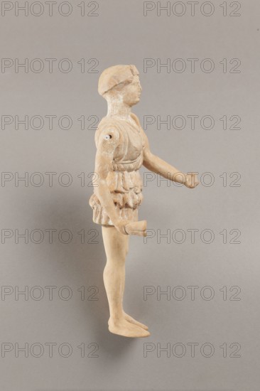 Doll with movable limbs, terracotta, dolls, Made of terracotta. The doll with movable limbs depicts a woman in a short, pleated chiton and a bonnet. In her right hand she holds an instrument resembling castanets. The figure's oval head, directed slightly upwards, is set on a long, rather thick neck compared to the rest of the body. Lush curls protrude from under the headdress. The figurine's movable limbs are long compared to the rest of the body. 4th century BC, Attica according to Weronika Krzemien the object comes from Italy. Figurine, toy. Height 18.9 cm, width 8 cm, depth 3.5 cm, weight 0.13 kg., A standing figurine viewed in profile with a light tan to beige surface showing some pale white areas, wearing a textured garment around the torso and hips with sculpted folds, a rounded head with a simple cap or hair shape, an extended arm with a hand shaped into a partial grasp, the other arm bent at the elbow holding a short cylindrical object, smooth legs and flat feet, photographed a...