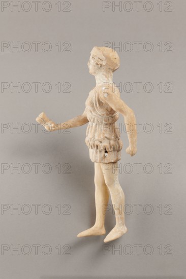 Doll with movable limbs, terracotta, made of terracotta. The doll with movable limbs depicts a woman in a short, pleated chiton and a bonnet. In her right hand she holds an instrument resembling castanets. The figure's oval head, directed slightly upwards, is set on a long, rather thick neck compared to the rest of the body. Lush curls protrude from under the headdress. The figurine's movable limbs are long compared to the rest of the body. 4th century BC, Attica according to Weronika Krzemien the object comes from Italy. Figurine, toy. Height 18.9 cm, width 8 cm, depth 3.5 cm, weight 0.13 kg., A small sculpted figure standing on a neutral backdrop, shown in profile with a turned head; the figure has a rounded head and short hair, a sleeveless tunic with gathered folds at the waist and hem, articulated shoulders with visible joint pegs, one arm extended forward with a bent hand and the other arm relaxed at the side, slender legs and flat feet. The object displays a weathered surface wi...