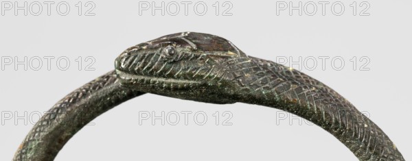 Snake bracelet, snakes, bracelets, 1st century BC, Italy, jewelry; height 2.3 cm, width 9.7 cm, depth 9 cm, weight 174 g;, A close-up of a curved metallic object shaped like a snake head and body with textured scale patterns, showing a raised eye and carved ridges along the snout and jaw; the surface displays a mix of dark green, brown, and hints of black with small areas of lighter discoloration and metallic sheen against a pale gray background.