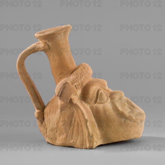 Vessel with a belly in the shape of a comic mask, unknown Greek workshop; plastic vessel with theatrical mask motif; Hellenistic period, 330–30 BC; Greece : vessel, height 10.6 cm, width 9 cm, depth 11.7 cm, weight 0.210 kg., A terracotta object in shades of light brown and tan shaped like a stylized human head with exaggerated facial features, showing a pronounced nose, brow, and closed mouth; a narrow neck rises from the top and connects to a curved handle that arches to the back, with textured surfaces and visible tool marks; the base is irregular and the piece casts a soft shadow on a neutral gray background.