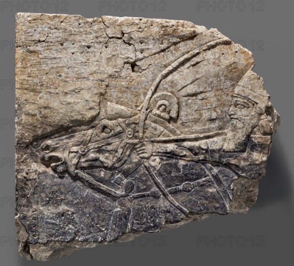 Fragment of an orthostat with relief decoration, unknown Neo-Assyrian workshop. Fragment of a stone wall-cladding slab orthostat with a relief representation of an archer on horseback. The realistically carved horse head, with a trimmed mane and a low horseshoe-shaped plume on top, features a meticulously rendered bridle. The rider, shown in left profile, holds a drawn bow with an arrow in his left hand and wears a helmet. As is customary, the eye is shown full face. The long beard and mustache are schematic and give the impression of being unfinished. In the upper left corner and between the bow and the rider's head are traces of an inscription having been chiseled off, indicating the slab's secondary use. Neo-Assyrian art, 7th century BC c. 668–c. 631 BC, reign of Ashurbanipal. From Kuyunjik ancient Nineveh, Southwestern Palace Palace of Sennacherib. Orthostat; height 28 cm, width 32 cm, depth 7.8 cm, weight 10.6 kg., A carved stone relief fragment showing part of a human figure faci...
