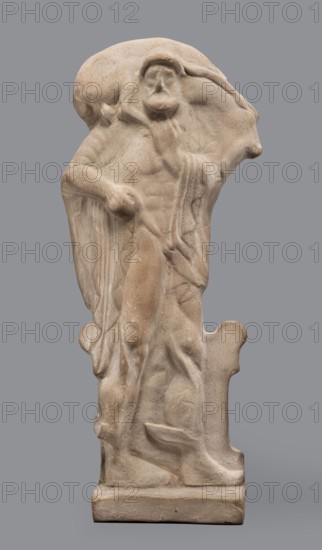 Figurine of Hermes Cryophorus, Statuette of Hermes Cryophorus striding to the right, carrying a goat on his back. His legs are decorated with wings. His face is framed by stubble and a pointed beard. With his left hand, he holds the goat's hind leg under his chin. The whole is depicted in a manner characteristic of the Archaic period: legs in profile, torso and head frontally. The god is depicted wearing a himation draped like a shawl over his shoulders, the ends falling down the sides. He wears a hairstyle with curls held above his forehead. Hermes strides on an altar, and his legs are depicted in relief against its background. In his bent left hand, he holds a caduceus. The whole is set on a small, rectangular base. 490–460 BC previously dated 500–490 BC; revised by analogy, Boeotia. Terracotta figurine; height 19.5 cm, width 9 cm, depth 4.5 cm, weight 0.28 kg., A carved stone figure in beige and light tan tones stands against a flat gray background, depicting a robed person with a r...