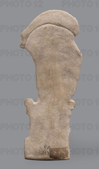Figurine of Hermes Cryophorus. Statuette of Hermes Cryophorus striding to the right, carrying a goat on his back. His legs are decorated with wings. His face is framed by stubble and a pointed beard. With his left hand, he holds the goat's hind leg under his chin. Depicted in a manner characteristic of the Archaic period: legs in profile, torso and head frontally. The god wears a himation draped like a shawl over his shoulders, the ends falling down the sides, and a hairstyle with curls held above his forehead. Hermes strides on an altar; his legs are depicted in relief against its background. In his bent left hand he holds a caduceus. The whole is set on a small rectangular base. Greek, Hermes mythology. Dated 490–460 BC previously 500–490 BC; revised to 490–460 BC. Origin: Boeotia. Terracotta figurine. Height 19.5 cm; width 9 cm; depth 4.5 cm; weight 0.28 kg., A roughly vertical carved stone object with an irregular, weathered surface and softened edges, shown against a flat gray bac...