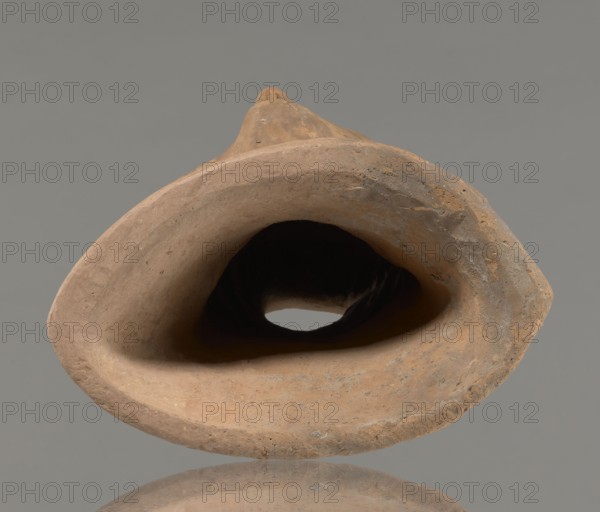 Votive female head, Female head wearing a wreath, from under which lush locks of hair curl down the sides of the face to the neck. High forehead, large eyes, deep-set in relation to the nose, slightly convex with developed eyelids and eyeballs, with marked pupils. Small, straight nose; narrow, slightly parted mouth with fleshy lips. Strong, slightly projecting chin; slim cheeks giving the face a triangular outline. 3rd–2nd century BC, Etruria; votive. Height 26 cm, width 21 cm, depth 13 cm, weight 2 kg., A close-up view of a hollow, rounded object made of rough clay with a matte surface, shown against a plain gray background; the clay displays shades of brown, tan, beige, and some dusty ochre, with darker brown in the deep interior and small areas of grayish discoloration on the outer rim; the object has an irregular oval opening leading into a shadowed cavity and shows textured, slightly pitted edges and subtle tool or hand-formed marks.