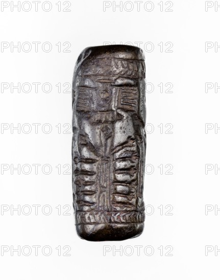Cylinder seal, unknown Neo-Assyrian workshop. Seal in the so-called linear style with a representation of a religious-magical scene of adoration of the holy tree in the form of a stylised pomegranate bush with a winged solar disc shown above. On both sides of the bush stand human figures in profile, dressed in identical long robes with fringes at the bottom. On the left is a priest, wearing a hat with a ribbon, on the right a king and a courtier, both without headgear. In the field behind the figures are symbols: a palm leaf and an eight-pointed star. The entire image is framed at the top and bottom with a herringbone ornament. Iconography: pomegranate bushes, winged discs, stars. Linear style. 9th–8th century BC; Neo-Assyrian period, Northern Mesopotamia place of manufacture; Assyria, Mesopotamia; Turkey, Syria, Iraq places of finding/origin. Cylinder seal; height 3.5 cm, width 1 cm., A small cylindrical carved object with a dark brown to nearly black surface showing polished highligh...