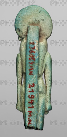 Amulet — figurine of a lion-headed goddess Sachmet?, Figurine of the goddess Sachmet with a lion's head topped with a solar disc with a uraeus, in a tripartite wig and a long narrow robe. The lower legs are missing, but the figure seems to be walking, with its arms lowered. On the back pillars. 664–332 BC; Late Period, Egypt. Amulet; height 5.8 cm, width 1.7 cm., A small vertical statuette photographed against a neutral gray background, showing the back of a standing human-like figure with an elongated straight back support and a large circular head; the surface has a weathered, grainy texture with areas of wear and small pits, and the predominant colors are turquoise and aqua with patches of pale green, sandy beige, and spots of darker green and brown; the figure has simplified arms hanging alongside the body and a slightly rounded base, and there is a vivid red-painted vertical marking along the back support that contrasts with the surrounding blue-green tones.