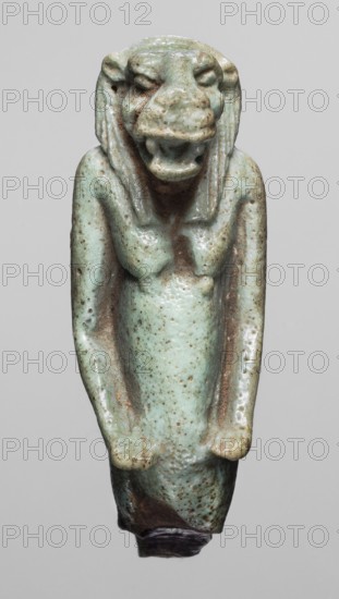 Amulet — Toeris Thoth?, Toeris myth., Egyptian deities, hippopotamuses, Egyptian religion; Late Period, 664–332 BC, Egypt; amulet, height 4.6 cm, width 1.5 cm., A small sculpted figure with a worn, glossy surface in shades of pale turquoise and light green with speckled brown spots, showing a stylized humanoid form with an animal-like head, a broad open mouth, and pronounced facial features; the figure has long slender arms held close to the body and a narrow torso that tapers toward the bottom, where a darker brown area is visible; the surface shows uneven texture and patina with areas of lighter green and darker brown discoloration against a neutral gray background.