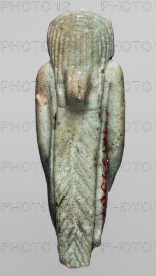 Amulet — Toeris; creator, Toeris myth.; Egyptian deities, hippopotamuses, Egyptian religion; Late Period, 664–332 BC, Egypt; amulet; height 4.6 cm, width 1.5 cm., A small carved figure shown from the back with a rounded head and textured vertical grooves suggesting hair, a protruding rectangular element at the upper back, long narrow arms resting along the sides, and a tapered lower body carved with chevron-like grooves; the surface shows a weathered, speckled pale green to bluish-green coloration with areas of brownish discoloration and small dark spots, and a few small accents of bright red on one side, all set against a plain light gray background.