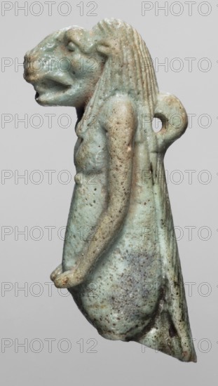 Amulet - Toeris, repossession Radom, Toeris myth., Egyptian deities, hippopotamuses, Egyptian religion, 664–332 BC; Late Period, Egypt, amulet, height 4.6 cm, width 1.5 cm, A small sculpted figure with a lion-like head and human torso seen in profile, rendered in a pale green-blue color with areas of light beige and brown spotting, showing textured hair with vertical ridges, a looped projection at the back, a partial arm extending forward with a rounded hand, a tapered lower body with rough pitted surface and darker speckling, and an overall worn, slightly glossy surface against a plain gray background.