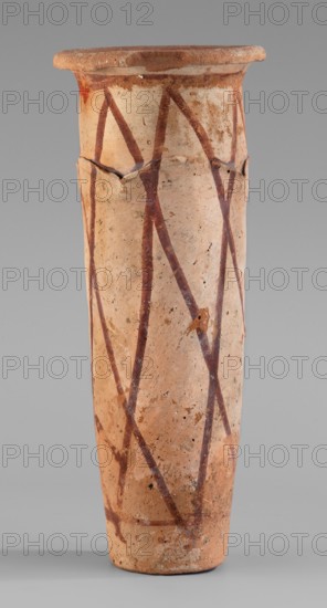 Cylindrical vessel with crosshatched decoration, painted vessels, Egyptian ceramics, engraved decorations, geometric motifs. The vessel has a shape resembling a cylinder, slightly tapering towards the bottom, with a slightly convex bottom, and a widely rolled-out rim. A plastic, wavy ornament runs 3/4 of the way up. It is arranged on the surface in such a way that the upper part of the vessel appears to be recessed relative to the lower. The surface is covered with a light engobe and decorated with a painted diagonal grid. B. Ruszczyc, c. 3200–c. 3050 BC; Predynastic Period, Naqada III Naqada phase IIIa2, Abusir el-Melek, vessel, height 27.5 cm, width 11 cm, weight 1.028 kg., A tall cylindrical ceramic vessel with a flared rim, showing a surface of beige and light tan clay with darker brownish-red painted zigzag line patterns around its body; the rim and upper edge have a slightly darker, more reddish-brown tone and there are areas of rough texture and small chips and cracks visible on...
