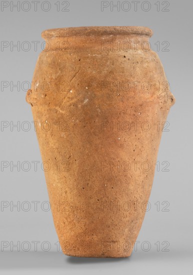 Vessel with wavy handles. Vessel with an elongated belly that widens towards the top. Short, cylindrical neck. Rounded, upturned rim. At approx. 2/3 of the height two residual vices are preserved, resembling an attached roller with a wavy profile. The vices are placed asymmetrically. Flat bottom. Surface even. Scratch marks visible in the upper part of the vessel. Clay color: light red. Egyptian ceramics; vessel for oils and ointments. c. 3500–3050 BC; Predynastic Period, Naqada II/III Naqada phase IId2–IIIa1. Abusir el-Melek findspot. Height 20.2 cm; width 13.3 cm; weight 0.708 kg., inscription/repository notes indicate repossession Bytom., A large terracotta-colored clay jar with a rounded rim and a tapered body standing against a neutral gray background; the surface shows a rough, slightly pitted texture with small pale speckles and subtle variations in brown and orange tones, and there are small protrusions on the sides near the shoulder.
