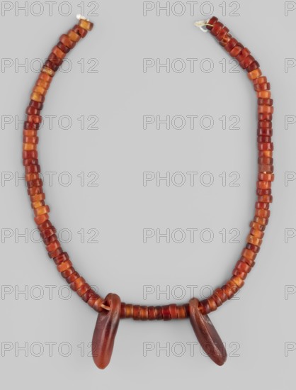 Necklace - fragment, cylindrical beads, Necklace of cylindrical beads interrupted by two pendants of elongated, irregular shape, in various shades of red, 5 thousand BC, Kadero grave no. 3, jewelry, height 25.2 cm, A beaded necklace arranged in a loose U shape against a light gray background, composed of a string of small cylindrical beads in shades of red, orange, and amber, with a few beads showing darker reddish-brown tones; two larger elongated pendant beads in darker reddish-brown hang from the lower center of the strand.