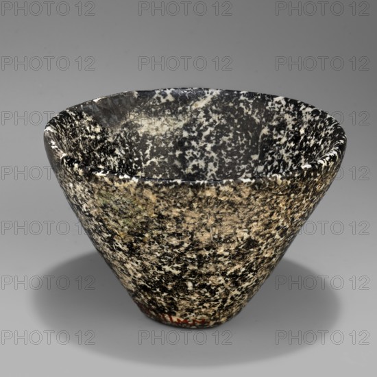 Bowl with high walls widening toward the top; rim rounded and slightly beveled inward; small flat bottom. Stone vessel, height 6.7 cm, width 4.9 cm, weight 0.30 kg. Ca. 3100–2686 BC, Early Dynastic Period, Egypt., A roughly conical bowl with a flared rim sits against a neutral background; the bowl's surface shows a speckled, mottled pattern in black, white, beige, and hints of green, creating a marbled appearance that continues inside and out, with a smooth, slightly glossy finish and a rounded interior edge visible around the rim.
