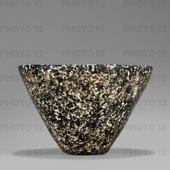 Bowl with high walls, widening towards the top. The rim is rounded and slightly beveled inwards. The bottom is small and flat. Stone vessel, ca. 3100–ca. 2686 BC Early Dynastic Period, Egypt., Vessel; height 6.7 cm, width 4.9 cm, weight 0.30 kg., A conical bowl with a speckled surface sits against a plain background; the bowl displays a mottled pattern of black, white, and beige tones across its exterior, with a rounded rim and a tapered base casting a soft shadow beneath it.