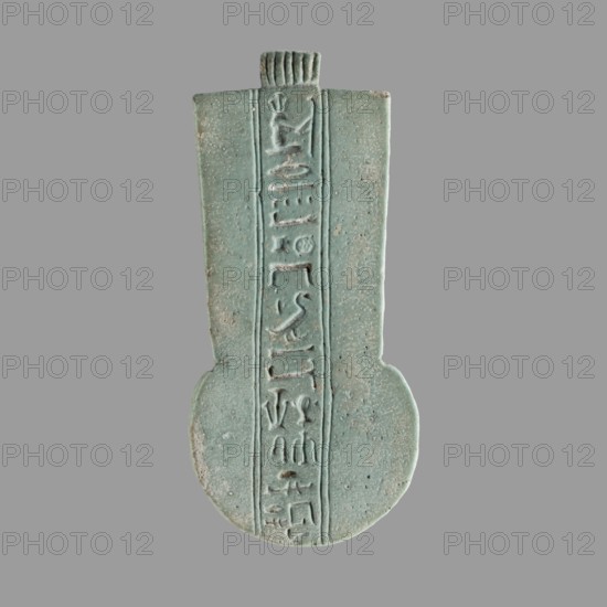 Amulet — weight of the menit necklace of the priest Achpet; menit weight with a central column of hieroglyphic inscription; hieroglyphs; priestly necklace weight; maker, Achpet ca. 664–404 BC; Late Period, Egypt 664–332 BC; amulet; height 8.7 cm, width 3.5 cm., A single vertical object with a rounded bottom and a narrower rectangular top sits against a neutral gray background; the object is primarily a muted turquoise-green with areas of lighter and darker greenish-blue and small pale spots, and it has a central vertical recessed strip bordered by raised edges containing a series of carved shapes and markings; the surface shows a slightly rough, pitted texture and worn edges with subtle beige and off-white wear at some high points.