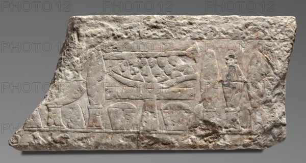 Relief from the mortuary temple of Niuserre, Niuserre ruler of Egypt; ca. 2445–2421 BC, restitution provenance, offerings and ritual vessels iconography, architectural elements, religious scenes, funerary architecture. Fragment of a block with a high relief representation of an offering table and objects intended for sacrifice. ca. 2445–2421 BC; Old Kingdom, 5th Dynasty Nyuserre's reign, Abusir. Bas-relief; height 26 cm, width 53 cm, depth 10 cm, weight 21 kg., A roughly rectangular stone slab with an irregular, chipped edge displays shallow carved reliefs across its surface; the stone is primarily off-white and light beige with patches of pale gray and small areas of muted reddish-brown and faint greenish discoloration. The carved scenes include rounded and angular shapes suggesting vessels and a curved object resting on a horizontal support, with flanking column-like forms and a standing human-like figure on one side; the surface shows tool marks, weathering, and pitted rough areas, ...
