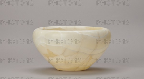 Bowl, large stone bowl with a small flat bottom, slightly flared side walls at the top bent inwards and a straight rim, ca. 2686–2181 BC, Old Kingdom, found at Abu Rawash, vessel, height 14 cm, width 23 cm, weight 1.35 kg, A smooth, rounded bowl with a matte surface sits against a plain background; the bowl shows a marbled pattern of pale cream and yellow tones with subtle banding and faint veins, and there are areas of slightly darker yellow and off-white creating irregular shapes across its curved exterior, while the background and surface beneath the bowl appear in muted gray and taupe shades.