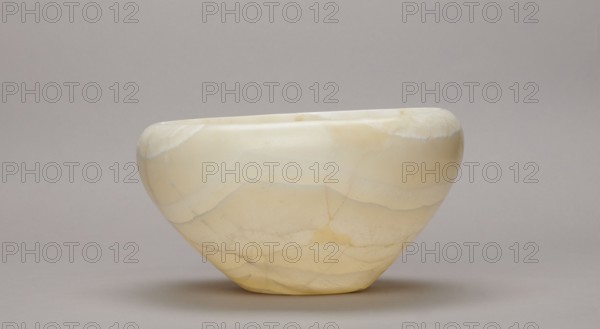 Bowl, stone vessel; large bowl with a small flat bottom, slightly flared side walls at the top bent inwards and a straight rim; Old Kingdom, ca. 2686–2181 BC; found at Abu Rawash; vessel, height 14 cm, width 23 cm, weight 1.35 kg., A smooth, rounded bowl-shaped object sits centered against a neutral background, displaying a pale cream to soft yellow color with subtle banding and veined patterns in slightly darker yellow and off-white tones; the surface appears polished and slightly reflective, with soft shadows beneath it and a muted gray-beige backdrop.