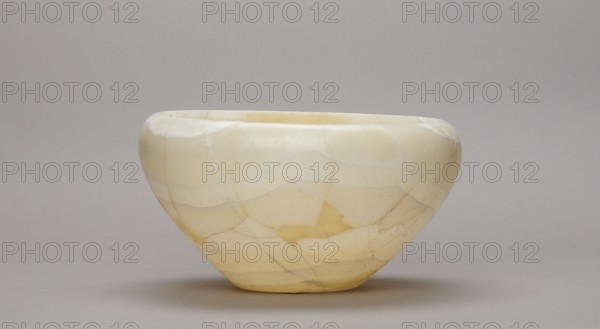 Bowl, large stone bowl with a small flat bottom, slightly flared side walls at the top bent inwards and a straight rim, ca. 2686–ca. 2181 BC Old Kingdom, found at Abu Rawash, vessel; height 14 cm, width 23 cm, weight 1.35 kg, A smooth rounded bowl with a wide rim and gently tapered base sits against a plain backdrop, showing a marbled surface with a glossy finish; the bowl displays a mix of pale cream, warm yellow, off-white, and light beige tones with subtle veining and patches of translucent color, and the background and surface beneath the bowl appear in muted gray and taupe shades.