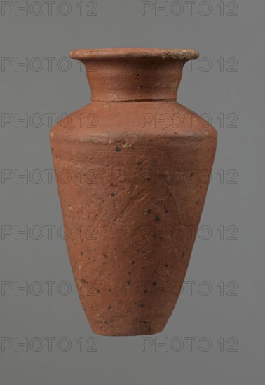 Vessel, Egyptian pottery, clay vessel, conical-shaped vessel, widest at approximately 3/4 of its height. Quite wide, almost horizontal shoulders—slightly sloping. Wide, short, funnel-shaped neck widening towards the spout. Wide spout, flat in the upper part, slightly rounded at the bottom, slightly asymmetrical. Flat, asymmetrical bottom. Surface leveled. Lower part finished to approximately 2/3 of its height with a knife or similar tool. Outer surface and inner surface of rim and neck covered with a layer of dark red engobe. Vessel color: dark red. Vessel complete; surface eroded in many places, numerous clay chips on the rim. Ca. 2686–ca. 2181 BC; Old Kingdom, Edfu. Vessel height 16 cm; diameter 8.6 cm rim, 10.7 cm body, 4.5 cm bottom., A single clay vessel with a rounded shoulder and a flared rim, shown centered against a plain gray background, has a rough textured surface with visible pitting and small dark speckles; the vessel is mainly terracotta red with patches of darker brown ...