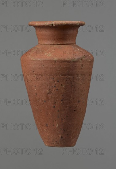 Vessel, Egyptian pottery, conical-shaped clay vessel, widest at ~3/4 of its height with wide, almost horizontal shoulders slightly sloping. Wide, short funnel-shaped neck widening toward the spout; wide spout flat on top, slightly rounded at bottom, slightly asymmetrical. Flat, asymmetrical bottom. Surface leveled; lower part finished to ~2/3 of its height with a knife or similar tool. Outer surface and inner surface of rim and neck covered with a layer of dark red engobe. Vessel color dark red. Vessel complete; surface eroded in many places, numerous clay chips on the rim. Old Kingdom, ca. 2686–ca. 2181 BC; Edfu. Dimensions: height 16 cm; diameter 8.6 cm rim, 10.7 cm body, 4.5 cm bottom. References: Rzeuska, p. 70, fig. 52, cat. 44., A single tall earthenware vessel with a narrow base and wider shoulder tapering to a short neck and flared rim, showing a rough textured surface with weathered patches and small pitted spots; the vessel is predominantly terracotta with flecks of darker br...