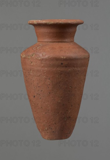 Vessel, Conical-shaped clay vessel, widest at approximately 3/4 of its height with quite wide, almost horizontal shoulders that slightly slope. Wide, short funnel-shaped neck widening toward the spout. Wide spout, flat in the upper part, slightly rounded at the bottom, slightly asymmetrical. Flat, asymmetrical bottom. Surface leveled; lower part finished to approximately 2/3 of its height with a knife or similar tool. Outer surface and inner surface of the rim and neck covered with a layer of dark red engobe. Vessel color: dark red. Vessel complete; surface eroded in many places, numerous clay chips on the rim. Dated ca. 2686–ca. 2181 BC Old Kingdom, Edfu. Height 16 cm; diameter 8.6 cm rim, 10.7 cm body, 4.5 cm bottom., A single terracotta-colored clay vessel with a flared rim and a tapered body is centered against a neutral gray background; the vessel shows a textured, slightly rough surface with darker speckles and lighter patches of wear, and colors visible include terracotta, darke...