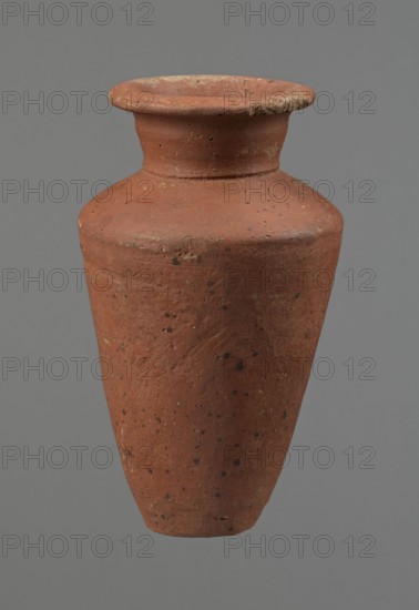Vessel, Egyptian pottery, ceramics, clay vessel. Conical-shaped vessel, widest at approximately 3/4 of its height. Quite wide, almost horizontal shoulders - slightly sloping. Wide, short, funnel-shaped neck, widening towards the spout. Wide spout, flat in the upper part, slightly rounded at the bottom, slightly asymmetrical. Flat, asymmetrical bottom. Surface leveled. Lower part finished to approximately 2/3 of its height with a knife or similar tool. Outer surface and inner surface of the rim and neck covered with a layer of dark red engobe. Vessel color dark red. Vessel complete; surface eroded in many places, numerous clay chips on the rim. Ca. 2686–ca. 2181 BC; Old Kingdom, Edfu, vessel; height 16 cm, diameter 8.6 cm rim, diameter 10.7 cm body, diameter 4.5 cm bottom., A single terracotta vessel fills the frame, showing a wide flared rim leading to a short neck and a rounded shoulder that tapers into a conical body; the surface is rough with a weathered texture and scattered darker...