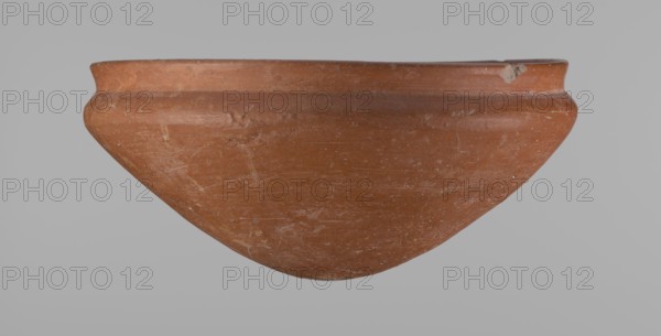 Medum type bowl, Medum type bowl with carination under the rim. Rim diameter smaller than the diameter of the shoulders. Rounded bottom. Straight, slightly flaring rim. Vessel made on the wheel of Nile clay, surface leveled. The bottom and lower part of the vessel finished to about half its height with a knife or similar tool. The surface of the vessel is covered with a layer of engobe . Vessel colour – red. c. 2686–c. 2181 BC, Old Kingdom, Edfu. Vessel; height 9 cm; diameter 21.1 cm rim, 21.5 cm shoulders., A broad, shallow bowl-shaped ceramic object with a rounded base and a slightly flared rim sits against a plain light gray background; the surface of the object is a warm terracotta color with areas of lighter and darker reddish-brown, showing a weathered texture with scratches and small worn spots, and there is a noticeable small chip on the rim revealing a paler interior.