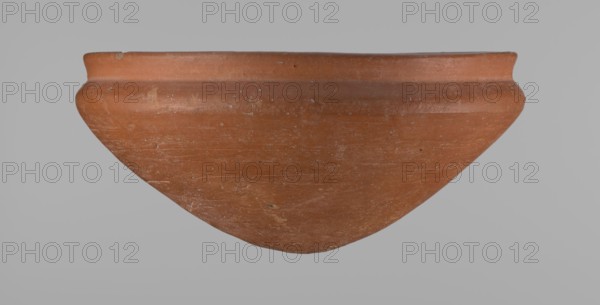 Medum type bowl, Ceramics; Egyptian pottery vessel Medum type bowl with carination under the rim. Rim diameter smaller than the diameter of the shoulders. Rounded bottom. Straight, slightly flaring rim. Made on the wheel from Nile clay; surface leveled. Bottom and lower part finished to about half its height with a knife or similar tool. Surface covered with a layer of engobe . Vessel color: red. Date: c. 2686–c. 2181 BC Old Kingdom. Origin: Edfu. Function: vessel. Height 9 cm; diameter rim 21.1 cm; diameter shoulders 21.5 cm., A large shallow bowl-like clay vessel is shown against a plain light gray background, with a rounded body tapering to a blunt point and a slightly flared rim; the surface shows a weathered texture with scratches and small chips. The predominant color of the vessel is terracotta, with lighter and darker variations of reddish-brown and some pale tan spots.
