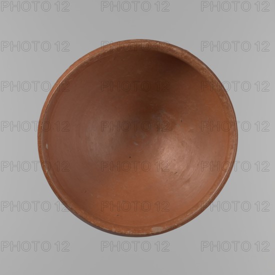 Medum type bowl, Medum type bowl with carination under the rim. Rim diameter smaller than the diameter of the shoulders. Rounded bottom. Straight, slightly flaring rim. Vessel made on the wheel of Nile clay, surface leveled. The bottom and lower part of the vessel finished to about half its height with a knife or similar tool. The surface of the vessel is covered with a layer of engobe . Vessel colour – red. c. 2686–c. 2181 BC; Old Kingdom, Edfu. Vessel; height 9 cm, diameter 21.1 cm rim, diameter 21.5 cm shoulders, A top-down view of a round, shallow clay bowl in a reddish-brown color with a smooth interior surface and subtle variations in tone, placed against a light gray background; the bowl shows a worn rim with small chips and scuffs, and there are a few tiny dark specks and faint discolorations inside.