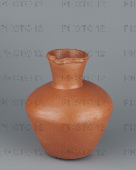 Jug. Medium-sized biconical clay jug with wide, rather sloping shoulders and a wide neck that is almost cylindrical in its lower section and widens toward the spout, the neck’s height about one-third of the vessel. Profiled, irregular spout raised and extended on one side to form a small secondary spout; slightly rounded, almost triangular in cross-section, with a small indentation on the outer profile. Body widest at about half its height; bottom almost flat, very slightly rounded. Wheel-made from Nile clay NB1 Vienna System. Outer surface leveled, covered with engobe and polished; inner surface leveled. Red-brown color. Complete, very well preserved. Old Kingdom, 5th–6th Dynasty, c. 2494–c. 2181 BC. Findplace: Edfu. Vessel. Height 19.9 cm; rim dia. 8.1 cm; bottom dia. 9.5 cm; body dia. 16.7 cm; weight 1.1 kg. Comparable examples: T. Rzeuska, Saqqara II, pl. 54, cat. 210; G. Brunton, Qau and Badari, pl. XLII, 661 V; analogous vessel in the Louvre., A terracotta-colored rounded clay ve...