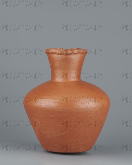 Jug. Medium-sized biconical clay jug, widest at about half its height with wide, sloping shoulders. Wide neck nearly cylindrical in its lower section, widening toward the spout; neck height about one-third of total vessel height. Profiled, irregular spout raised and extended on one side forming a small secondary spout; slightly rounded, almost triangular in cross-section with a millimetre-long indentation on the outer profile. Bottom almost flat, very slightly rounded. Made on the wheel of Nile clay NB1, Vienna System. Outer surface leveled, covered with an engobe and polished; inner surface leveled. Red-brown color. Complete, very well preserved. Old Kingdom, 5th–6th Dynasty c. 2494–c. 2181 BC, Edfu. Vessel; height 19.9 cm; rim dia. 8.1 cm; bottom dia. 9.5 cm; body dia. 16.7 cm; weight 1.1 kg. References to analogous examples: T. Rzeuska Saqqara II and G. Brunton Qau and Badari; an analogous vessel from Edfu is in the Louvre., A plain terracotta vessel with a rounded body narrowing to...