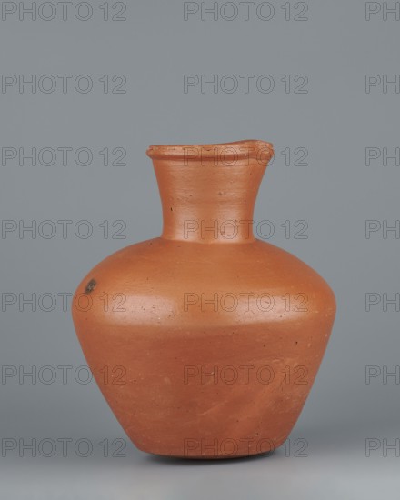 Jug. Medium-sized biconical clay jug with wide, rather sloping shoulders and a wide neck that is almost cylindrical in its lower section and widens toward the spout; the neck is about one-third of the vessel’s height. Profiled, irregular spout, raised and extended on one side forming a small secondary spout; slightly rounded, almost triangular in cross-section, with a shallow millimetre-long indentation on the outer profile. Bottom almost flat, very slightly rounded. Made on the wheel of Nile clay NB1 Vienna System. Outer surface leveled, covered with an engobe and polished; inner surface leveled. Red-brown color. Complete and very well preserved. Analogous examples published by T. Rzeuska Saqqara II and G. Brunton Qau and Badari; an analogous vessel from Edfu is dated c. 2494–c. 2181 BC, Old Kingdom, 5th–6th Dynasty. Vessel: height 19.9 cm; rim diameter 8.1 cm; bottom diameter 9.5 cm; body diameter 16.7 cm; weight 1.1 kg., A terracotta-colored rounded pot with a bulbous body and a sli...