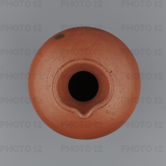 Jug, Medium-sized biconical clay jug with wide sloping shoulders and a wide neck that is almost cylindrical in its lower section and widens toward the spout. The spout is profiled and irregular, raised and extended on one side to form a small secondary spout; it is slightly rounded, nearly triangular in cross-section, with an approximate millimetre-long indentation on the outer profile. Vessel is widest at about half its height; bottom nearly flat, very slightly rounded. Made on the wheel from Nile clay NB1 Vienna System. Outer surface leveled, covered with an engobe and polished; inner surface leveled. Red-brown color. Complete and very well preserved. Date: c. 2494–c. 2181 BC, Old Kingdom, 5th–6th Dynasty, from Edfu. Function: vessel. Dimensions: height 19.9 cm; rim diameter 8.1 cm; bottom diameter 9.5 cm; body diameter 16.7 cm; weight 1.1 kg. Analogies: T. Rzeuska, Saqqara II; G. Brunton, Qau and Badari., A round terracotta object viewed from above with a central circular opening an...