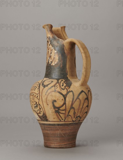 Red-figure oinochoe by the Pennsylvania Torcop Painter, Classified Gallo-Classic Scenography; red-figure decoration of wine vessel depicting mythological scenes and women; 2nd half of the 4th–3rd century BC circa 300–280 BC, to be verified; Etruria provenance; vessel; height 31.5 cm, width 16.2 cm, depth 15.6 cm, weight 0.94 kg., A ceramic jug with a rounded body, a narrow neck with a flared double spout, and a curved handle joining the neck and shoulder, all resting on a tapered foot; the surface shows painted decorative motifs in dark brown to black on a light tan to beige background, with areas of darker brown near the base and neck, and small spots of white paint in a patterned area; the decoration includes flowing curved lines and stylized floral or leaf-like shapes around the body and a crosshatched or lattice pattern near the neck; the overall color palette includes tan, beige, dark brown, black, and touches of white, set against a neutral gray studio backdrop.
