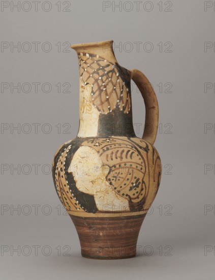 Red-figure oinochoe by the Pennsylvania Torcop Painter, Classified Gallo-Classic Scenography; red-figure pottery, wine vessel depicting mythological scenes and women; 2nd half of the 4th–3rd century BC ca. 300–280 BC, to be verified; Etruria place of origin; vessel; height 31.5 cm, width 16.2 cm, depth 15.6 cm, weight 0.94 kg., A painted ceramic jug with a rounded body, narrow neck, and single curved handle, shown against a plain gray background; the jug has an overall beige and tan base color with areas of black and dark brown paint, white painted dots and pale cream painted regions, and reddish-brown horizontal bands near the foot; decorative patterns include curved and looping lines, dotted accents, and a stylized profile-like pale shape on the body, with a netlike dark pattern on the neck and a smoothly curved handle colored tan with darkened spots.