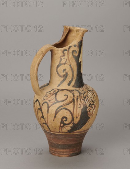 Red-figure oinochoe by the Pennsylvania Torcop Painter, Classified Gallo-Classic Scenography; red-figure pottery, vessel for wine depicting mythological scenes and women; 2nd half of the 4th–3rd century BC c. 300–280 BC, to be verified; Etruria place of origin; vessel; height 31.5 cm, width 16.2 cm, depth 15.6 cm, weight 0.94 kg., A ceramic jug with an elongated neck, rounded body, and a curved handle connecting the neck to the shoulder, displayed against a plain background; the jug's surface is primarily tan with areas of darker brown and black painted swirling and floral-like motifs, a banded darker brown base, and subtle variations in the tan color where the glaze or clay shows wear.