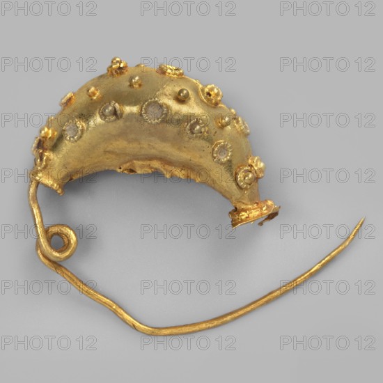 Leech fibula, brooch, goldsmithery. Leech fibula with a swollen ring made of gold plate, decorated with filigree rings with granulation in the center. No sheath. 6th century BC, Etruria. Jewelry, fibula. Height 1.7 cm, width 2.1 cm, depth 0.7 cm, weight 0.7 g., A crescent-shaped metallic object in gold tones rests on a neutral gray background, with a curved wire loop extending from one end and a long slender pin attached; the crescent surface has a textured, slightly irregular finish with a few raised rounded studs and several small circular settings, some of which hold pale, translucent elements, and there are tiny clustered bead-like decorations in gold tones around the rim.