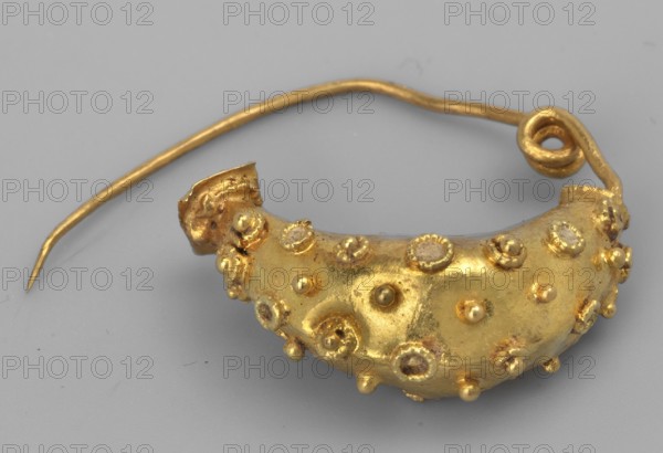 Leech fibula, brooch, goldsmithery. Leech fibula with a swollen ring made of gold plate, decorated with filigree rings with granulation in the center. No sheath. 6th century BC, Etruria. Jewelry, fibula. Height 1.7 cm, width 2.1 cm, depth 0.7 cm, weight 0.7 g., A close-up of a curved metallic object with a smooth gray background, showing a crescent-shaped gold piece hammered and decorated with a few raised round protrusions and rosette-like embellishments; a thin gold wire extends from one end, looping into a spiral and tapering to a pointed tip, and the visible colors are gold and gray.