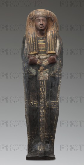 Lid of the sarcophagus of a man named Setau, Setau ca. 1479–1295 BC. Sacrificial formula and hieroglyphic inscriptions: a vertical band runs through the center, two columns along the edge of the lid, and three columns across the lid dividing the surface into six fields. The legs are clearly defined, the arms modeled, hands clenched. Chest bears a richly polychrome seven-row necklace; below the hand is a depiction of the winged goddess Nut. The head is sculpturally detailed: face painted red with large almond-shaped eyes set slightly obliquely; eyeballs clearly defined; pupils and eyebrows highlighted in black; straight, strongly flattened nose; small mouth with wide, full lips. Wig schematically decorated with yellow stripes. Face and hairstyle painted black, rendered in the round. A thin curved beard was formerly present visible in pre-war photo. c. 1479–c. 1295 BC; New Kingdom, late 18th Dynasty, Deir el-Medina tomb 1352, western necropolis; sarcophagus lid; height 192 cm, width 50 c...