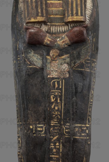 Lid of the sarcophagus of a man named Setau, Setau ca. 1479–1295 BC. Sacrificial formulas, Nut winged goddess, hieroglyphs; necklace iconographic, bracelet iconographic. A vertical band of inscription runs through the center – the sacrificial formula. Two columns of text along the edge of the lid and three columns of inscription across the lid divide the surface into six fields. The legs are clearly defined, the arms are modeled, the hands are clenched. On the chest is a richly polychrome seven-row necklace. Below the hand is a depiction of the winged goddess Nut. The head is sculpturally detailed: face painted red with large, almond-shaped eyes set slightly obliquely; eyeballs clearly defined; pupils and eyebrows highlighted with black paint. The nose is straight and strongly flattened; the mouth is small with wide, full lips. The wig is schematically decorated with yellow stripes. Setau once had a thin, curved beard visible in a pre-war photo. c. 1479–c. 1295 BC; New Kingdom, late 18...