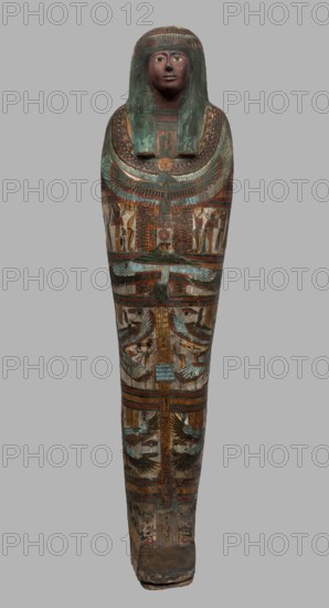 Mummy of Panepi in a cartonnage, doorkeeper of the temple of Amun Panepi, Panepi ca. 945–715 BC. Richly decorated cartonnage with sculpturally detailed wig and mask. On the chest is a necklace with plant and geometric ornament; below is a centrally located i3-w fetish mounted on a djed sign, behind which an inscription begins. Flanking the fetish are winged goddesses Isis and Nephthys and the Horuses of Edfu. At the base of the fetish are depictions of Upwawet. Above the fetish is a ram-headed bird with outstretched wings Amun-Ra and Wadjet cobra, Osiris, and three Sons of Horus. The deceased's hands are not modeled. c. 825–715 BC; Third Intermediate Period, late 22nd–23rd Dynasty, Western Thebes. Sarcophagus/mummy cartonnage. Height 170 cm; width 40 cm; depth 29 cm; weight 37.5 kg., The image shows a tall, elongated painted wooden sarcophagus with a stylized human face and wig at the top; the face and wig area display muted red, dark brown, and green tones, with the wig having patches...