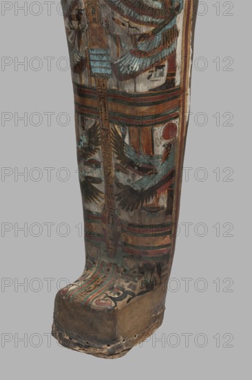 Mummy of Panepi in a cartonnage, doorkeeper of the temple of Amun Panepi, Panepi ca. 945–715 BC. Richly decorated cartonnage. The deceased's wig and mask are sculpturally detailed. On the chest is a necklace with plant and geometric ornament. Below is a centrally located i3-w fetish mounted on a djed sign, behind which an inscription begins. On the sides of the fetish are winged goddesses Isis and Nephthys and the Horuses of Edfu. At the base of the fetish are depictions of Upuaut. Above the fetish is a depiction of a ram-headed bird with outstretched wings Amun-Ra and Wadjet cobra, Osiris, and three Sons of Horus. The deceased's hands are not modeled. c. 825–715 BC; Third Intermediate Period, late 22nd–23rd Dynasty, Western Thebes. Sarcophagus/mummy cartonnage. Height 170 cm; width 40 cm; depth 29 cm; weight 37.5 kg., A tall painted wooden object with a curved foot and elongated lower leg section, decorated with bands and figurative motifs in muted tones of brown, teal, green, red, bl...