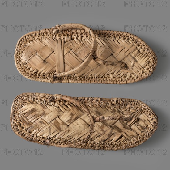 Sandals, pair of papyrus sandals made using the ribbon technique; edges finished with a cross-ribbed technique. Footwear; grave goods. New Kingdom, Egypt, c. 1550–c. 1069 BC. Clothing. Height 24.4 cm, width 11 cm., A pair of woven sandals made from natural fibers, displayed flat on a smooth gray background, showing a few areas of frayed and worn weaving; the sandals are tan and light brown with variations in shade across the woven strips and braided edges, and the straps are formed from twisted fiber loops.