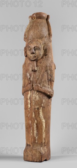Papyrus container - figure of the god Ptah-Sokar-Osiris, Atef crown with narrow feathers on a tripartite wig. Oval, wide face; straight long nose; large mouth with fleshy lips; large ears; straight beard. Arms modeled, folded on the chest, holding two nechacha whips. Torso wrapped in a shroud. Under the feet a large oval hole for inserting the papyrus plugged. On the back of the legs, fragment of an inscription painted in black, yellow, and red on a white background. Ptah-Sokar-Osiris mythology. Type II E according to Raven, ca. 1295–ca. 945 BC; 19th–21st Dynasty, Egypt. Sculpture; papyri/material culture. Height 60 cm, width 13.5 cm, depth 14 cm, weight 1.736 kg., A carved wooden figure with a tall headdress and a rounded top, showing a humanlike face with closed or downcast eyes and a small mouth, a short beard or chin piece, and ears carved at the sides; the figure's arms are crossed or held close to the chest and the body tapers into a long rectangular lower section. The surface sh...
