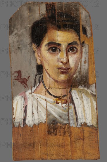 Mummy portrait of a boy. Portrait of a boy painted on a small board with diagonally cut upper corners. The boy, shown halfway down his torso, has his head tilted slightly to the left. Lush black hair, combed upwards, falls behind his right ear, creating a lock of youth. Facial features are carefully depicted: large eyes with light brown pupils, precisely modeled; defined eyelashes; a long straight nose; a small mouth with slightly downturned corners. He wears a white tunic with a trapezoidal neckline, a purple clarus coat over his right shoulder, and a white cloak slung over his left. A black ribbon terminating in a gold pendant hangs around his neck. Above the right shoulder, against a light brown background, is the figurine of a small dark brown horse breaking into a gallop. The gray background around the head is carelessly painted, with visible brush marks. 2nd half of the 2nd century according to K. Parlaski, late 1st century, perhaps first half of the 2nd century. Egypt; Fayum. Po...