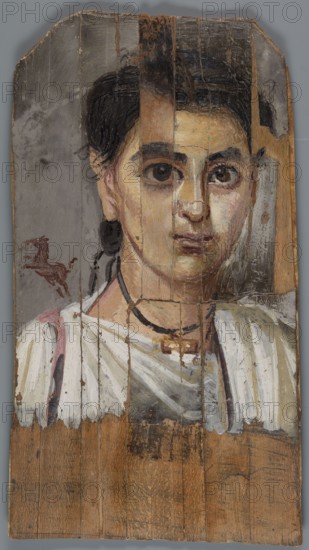 Mummy portrait of a boy. Portrait of a boy painted on a small board with diagonally cut upper corners. The boy, shown halfway down his torso, has his head tilted slightly to the left. Lush black hair, combed upwards, falls behind his right ear, creating a lock of youth. Facial features are carefully depicted: large eyes with light brown pupils, precisely modeled; defined eyelashes; a long straight nose; a small mouth with slightly downturned corners. He wears a white tunic with a trapezoidal neckline; a purple clarus coat over his right shoulder; and a white cloak slung over his left. A black ribbon terminating in a gold pendant hangs around his neck. Above the right shoulder, against a light brown background, is the figurine of a small dark brown horse breaking into a gallop. The gray background around the head is carelessly painted, with visible brush marks. 2nd half of the 2nd century according to K. Parlaski, late 1st century, perhaps first half of the 2nd century. Egypt; Fayum. Po...