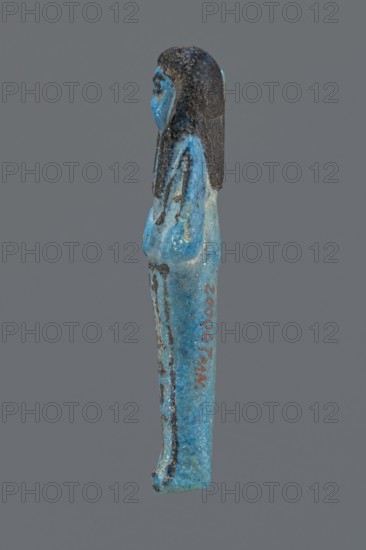 Ushabti Henut-netjeru, Henut-netjeru private name. Mummy-shaped figurine, grave good; shabti. Arms crossed on the chest, right over left, holding hoes in both hands. Rectangular basket on the back; painted tools. Wearing a usech necklace and wide bracelets; painted jewelry. Long, smooth three-part wig covering the ears; round face with large eyes, nose and mouth barely visible; wig and facial details painted. Painted inscription in one column on the front of the legs: Shd Osiris Henut-netjeru, justified by the voice. Date ca. 1069–945 BC; Third Intermediate Period, 21st Dynasty, Egypt. Dimensions: height 9 cm, width 3 cm, depth 1.5 cm., A small statuette of a standing figure shown in profile with a few shades of blue and black, the figure's body and clothing in bright turquoise-blue with darker blue speckling and a few black painted lines, the hair and upper head in a textured black, and a plain neutral gray background.